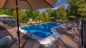 A swimming pool with lounge chairs and umbrellas, surrounded by trees and a brick deck. - Lake George 5 Bed/ 3 Bath home w/ lake & resort access (Lake George)