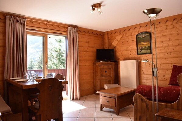 A wooden cabin interior with a dining table, chairs, a TV on a cabinet, a bed with a red pillow, and a floor lamp. - 50m from ski slopes, 2nd floor, swimming pool, balcony, tv, 44m², Méribel (Méribel - Les Allues)