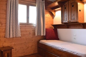 A wooden cabin room with a bed, a window with curtains, a small table, and a cabinet with a heart decoration. - 50m from ski slopes, 2nd floor, swimming pool, balcony, tv, 44m², Méribel (Méribel - Les Allues)