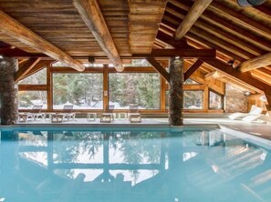 An indoor swimming pool with wooden beams and stone pillars, surrounded by lounge chairs and large windows offering a view of trees. - 50m from shops, 2nd floor, swimming pool, balcony, tv, 44m², Méribel (Méribel - Les Allues)