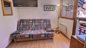 Une petite pièce accueillante, avec un canapé à motifs, une lampe sur pied et une fenêtre donnant sur les bâtiments environnants.