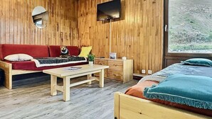 Une pièce chaleureuse avec un mur en bois, un canapé rouge, une petite table, un lit avec une literie bleue et un téléviseur fixé au mur.