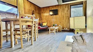 Une pièce chaleureuse avec des murs en bois, une table à manger avec des chaises, un canapé, un téléviseur et une grande fenêtre.