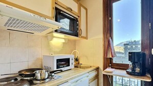 Une cuisine compacte équipée d’un four à micro-ondes, d’une cuisinière et d’un lave-vaisselle. Une fenêtre offre une vue sur les bâtiments et un ciel dégagé.