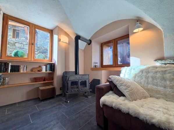 Una habitación acogedora con chimenea de piedra, un sofá con una manta de piel y una estantería llena de libros y objetos decorativos.