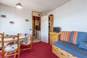 Um quarto acolhedor com mesa de jantar, cadeiras, sofá, televisão e cozinha.