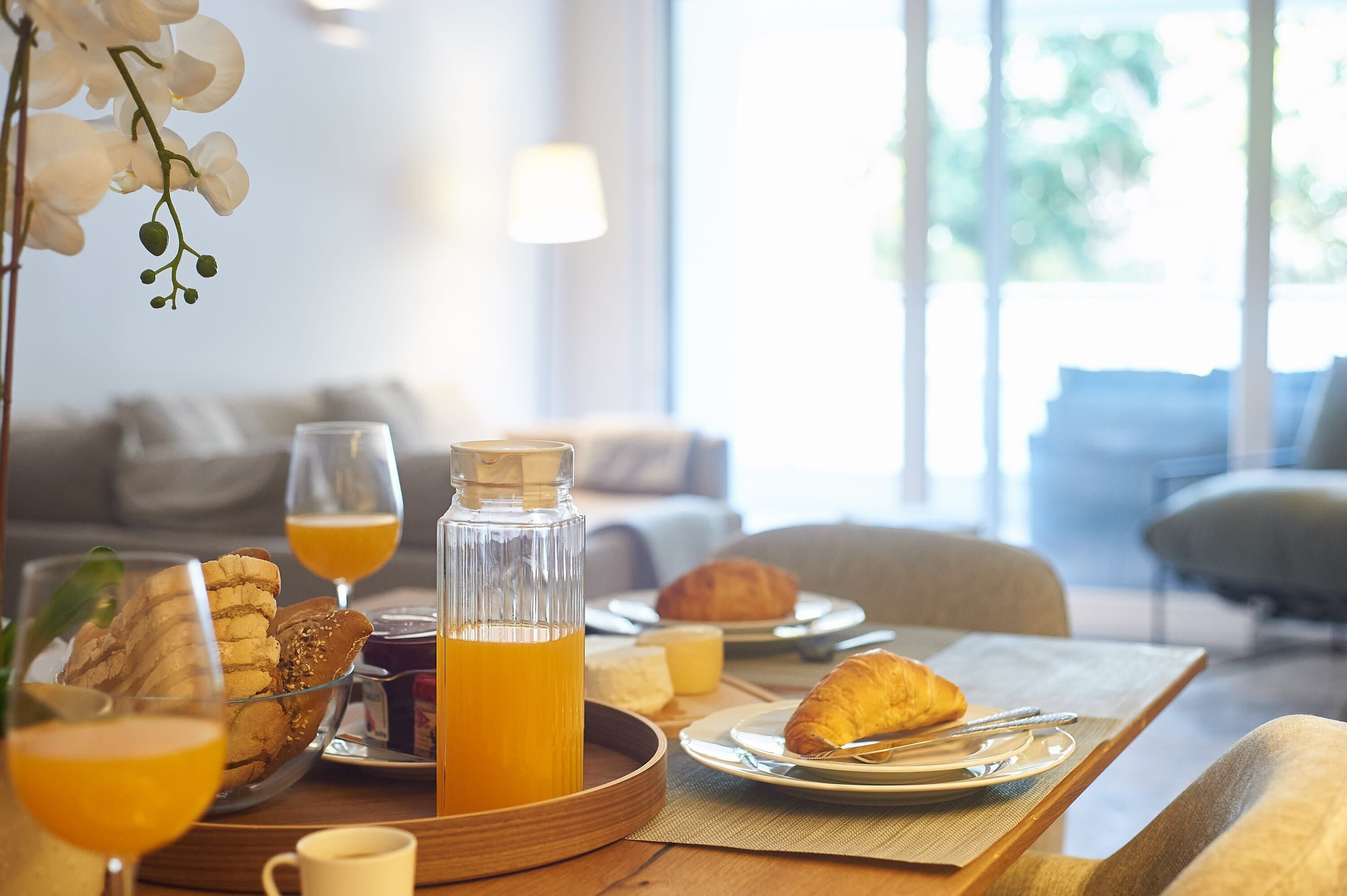 A breakfast setting with a glass bottle of orange juice, croissants, and pastries on a tray.