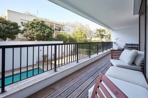 Un balcone con piscina, arredi da esterno e vista su edifici e alberi.