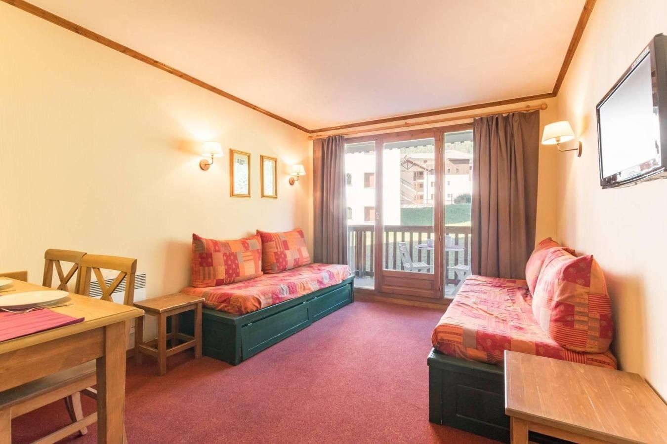 A room with a bed, a sofa, a table, and a chair. There is a balcony with a view of buildings.