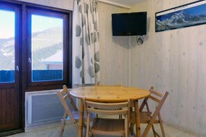 Enjoy meals at the dining table surrounded by comfortable chairs, with a flat-screen TV mounted above and a window offering a scenic mountain view.