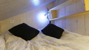 Kerrossänky, jossa on valkoiset vuodevaatteet ja mustat tyynyt, puuseinät ja kattovalaisin.