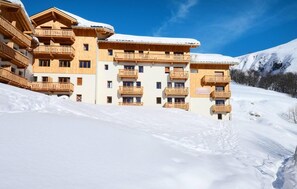Experience the serene tranquility of the mountains at LES BERGERS, where wooden balconies and a snow-covered roof blend seamlessly into the winter landscape.