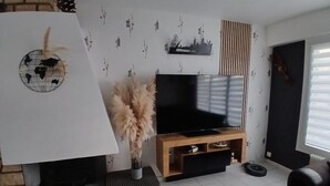 Een woonkamer met een open haard, een flatscreen televisie, een houten tv-meubel en een groot raam.