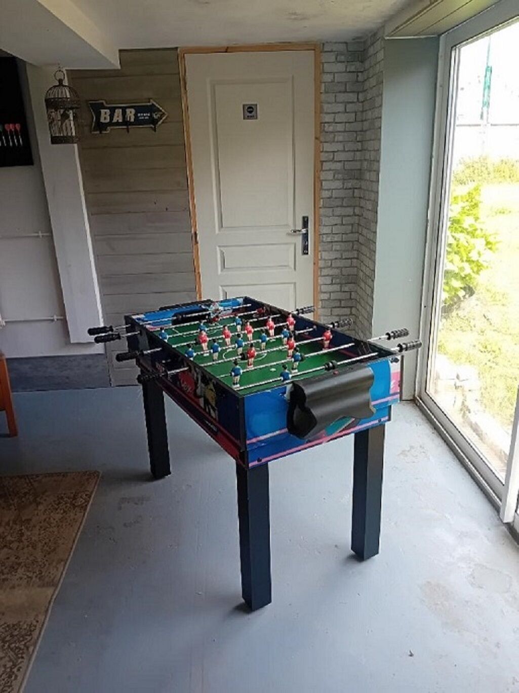 Ein Fußballtisch in einem Raum mit einer Tür, einem Fenster und einem Schild, das auf eine Bar hinweist.
