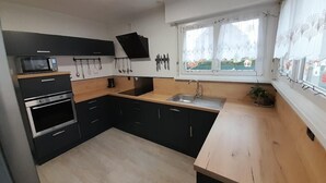Een moderne keuken met zwarte kastjes, een houten aanrecht, een ingebouwde oven, een magnetron en een raam met gordijnen.