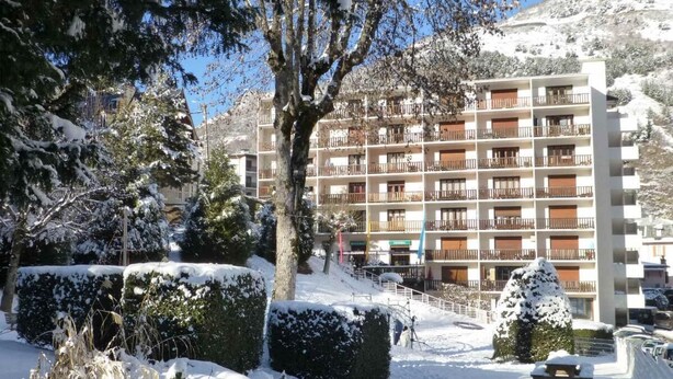 A multi-story hotel with balconies, surrounded by snow-covered trees and a mountainous backdrop.