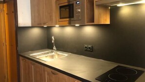 A kitchen with wooden cabinets, a stainless steel sink, a microwave, and an induction cooktop.