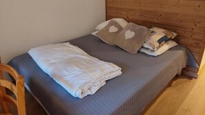 A single bed with a wooden headboard, a folded white blanket, and two pillows with heart designs.