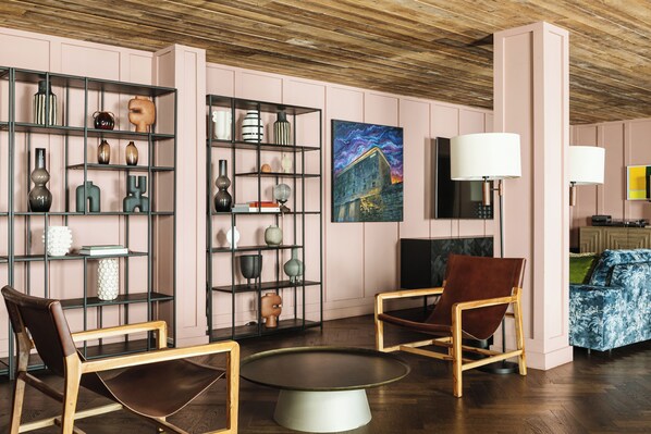 Una sala moderna con dos sillones de cuero, una mesa redonda para café y un televisor. Hay dos estantes con objetos decorativos y un cuadro en la pared.