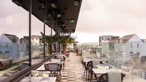 Una terraza con mesas y sillas, piso a cuadros y vistas a edificios.
