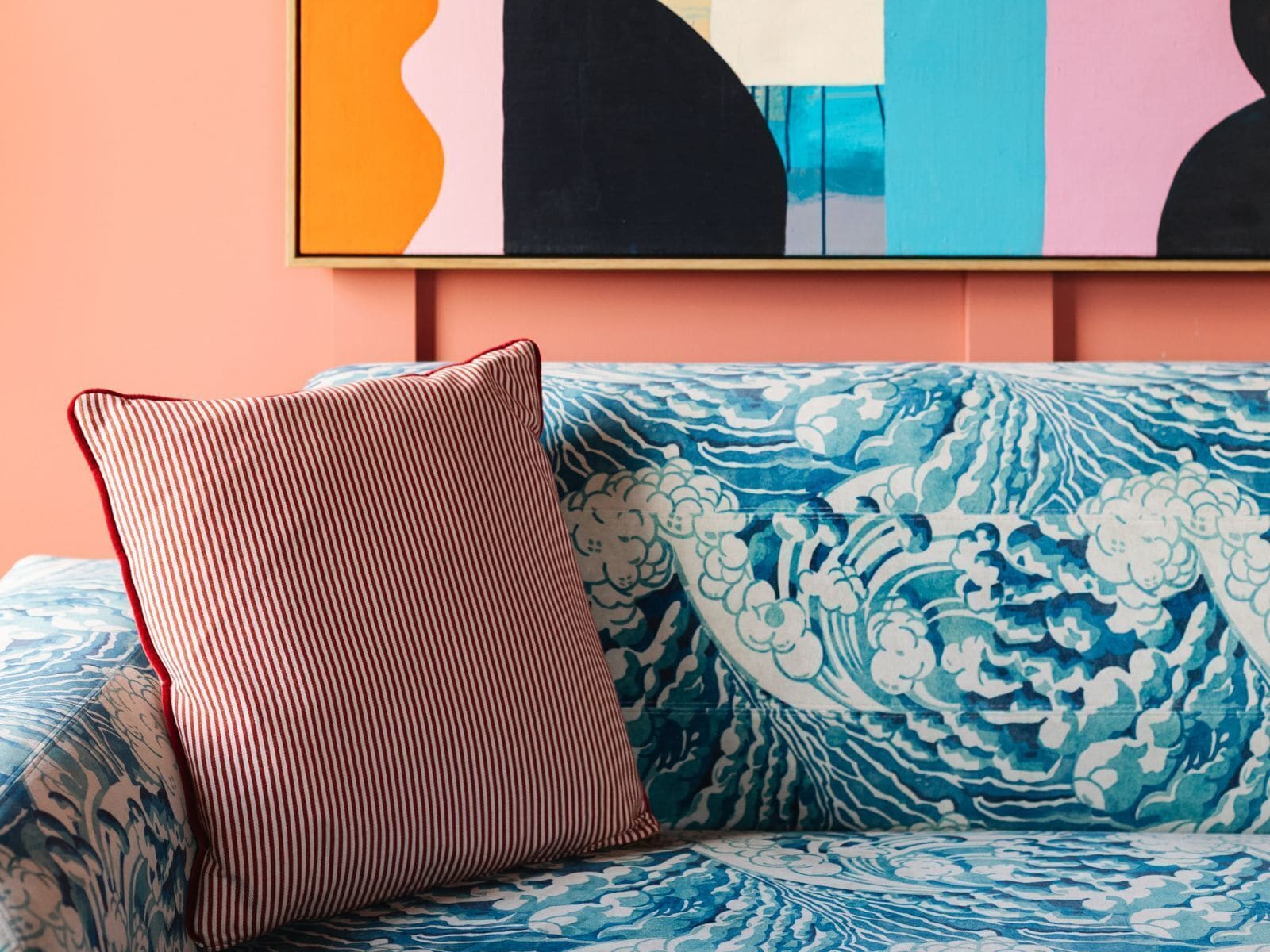 A blue patterned sofa with a striped pillow against a peach wall.