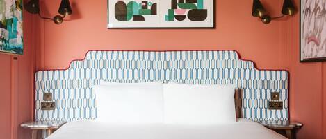 Un dormitorio con un cabecero estampado, una cama con ropa de cama blanca, dos mesitas de noche y lámparas de pared.