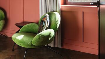 Un sillón verde con un cojín estampado, situado junto a una ventana con vistas a árboles.