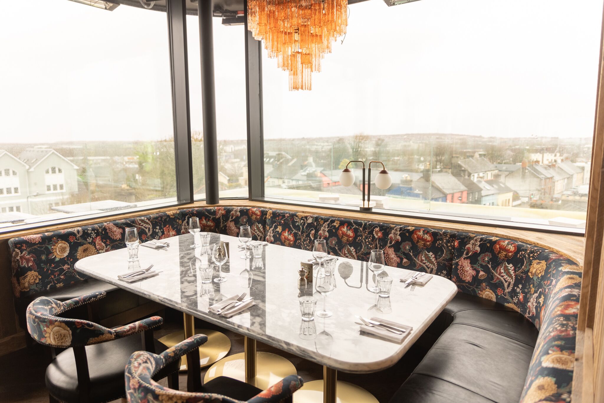 Un comedor con una mesa dispuesta para cuatro, asientos tipo cabina tapizados y vistas de la ciudad a través de amplias ventanas.