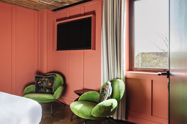 Una habitación con dos sillones verdes, un televisor de pantalla plana montado en la pared y una ventana con cortinas.