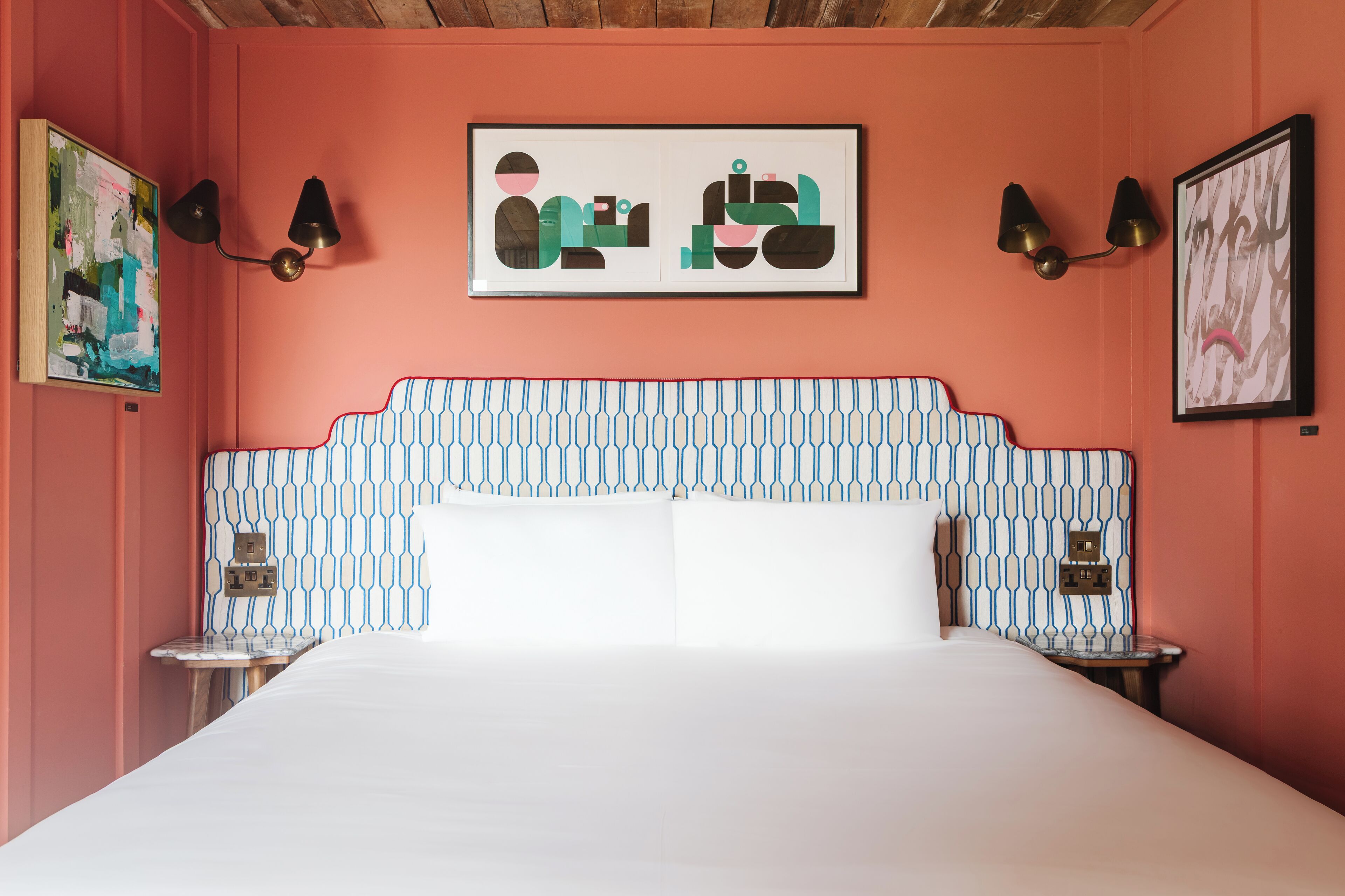 Ein Schlafzimmer mit einem gemusterten Kopfteil, zwei Nachttischen, einem Bett mit weißer Bettwäsche und Wandleuchten.