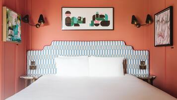 A bedroom with a patterned headboard, two bedside tables, a bed with white bedding, and wall-mounted lamps.