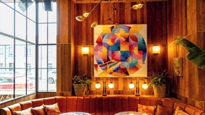 Un interior acogedor con una pared de madera, un cuadro abstracto colorido y un área de descanso con mesas.