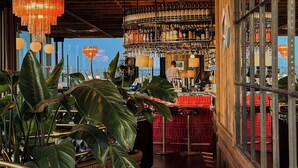 Zona de bar con vigas de madera, una lámpara de araña y una barra repleta de botellas.