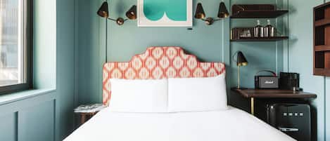 Un dormitorio ordenado con cama, mesita de noche, lámpara y una pequeña estantería con objetos.