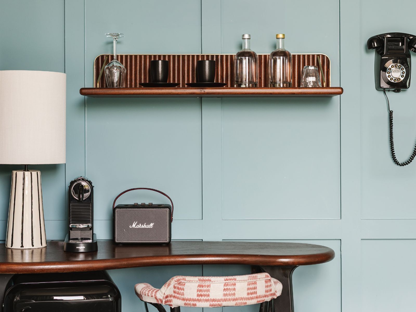 A vintage-style room with a wooden table, a radio, a telephone, and a shelf with bottles and glasses.
