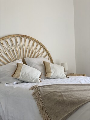 A bed with a rattan headboard, white pillows, and a beige throw blanket.