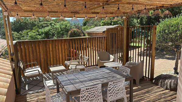 An outdoor patio with a wooden pergola, wicker hanging lamps, and a table with chairs. - Cosy accommodation, walking distance to the beach, sea-view patio. (Porto-Vecchio)