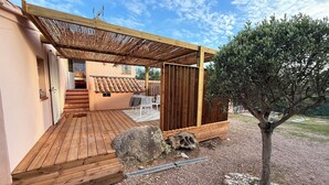 Una terraza de madera con una pérgola, un camino de piedra y un pequeño árbol.