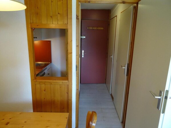 A narrow hallway with wooden paneling on the walls, a red door at the end, and a wooden bench in the foreground.