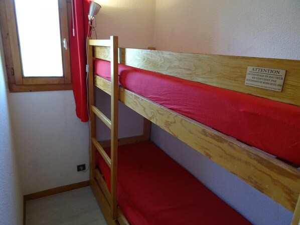 A bunk bed with a red mattress and a wooden frame. There is a ladder attached to the bed, and a sign on the wall above the bed.