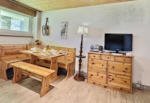 Un comedor de madera con bancos y una mesa dispuesta para dos personas, una lámpara, un televisor y una guitarra colgada en la pared.