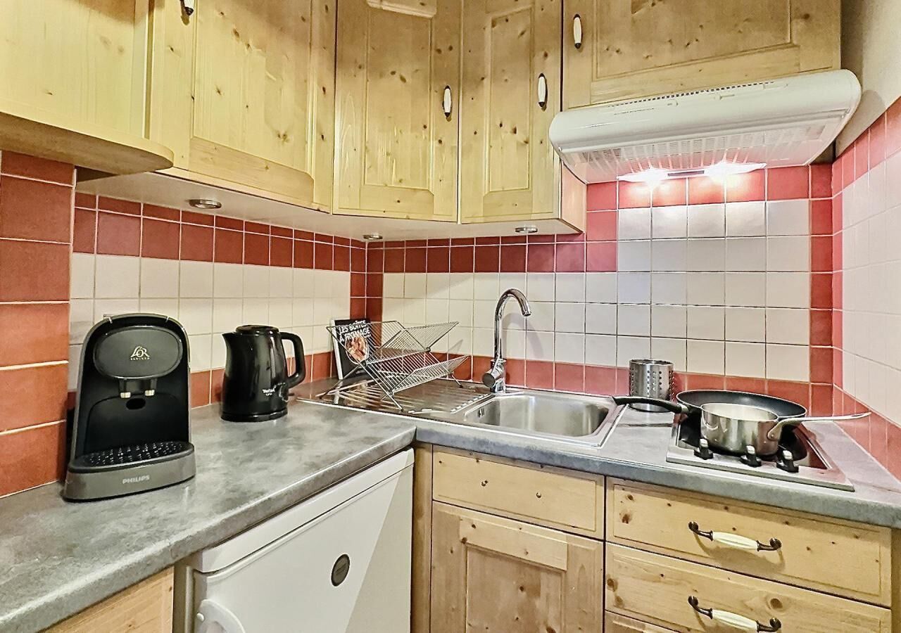 A compact kitchen with wooden cabinets, a coffee maker, a kettle, a sink, and a stove.