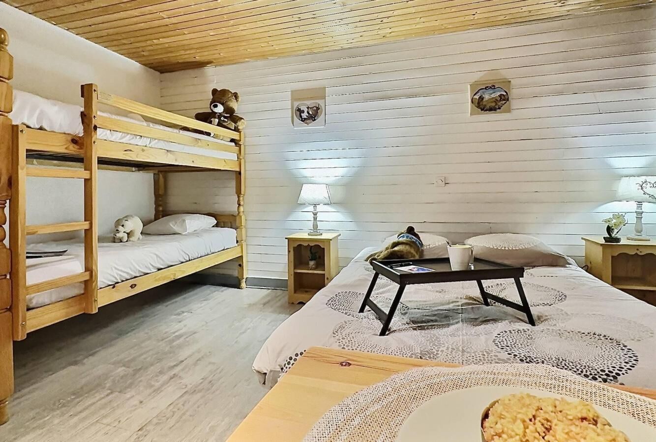 A bunk bed room with a wooden ceiling, a small table with a lamp, and a patterned rug.