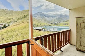 Un balcón con barandilla de madera que da a un paisaje montañoso con un lago y edificios.