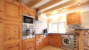 A kitchen with wooden cabinets, a built-in oven, a washing machine, and a window. - 100m from ski slopes, 1st floor, balcony, fireplace or stove, tv, ski locker, 90m², Val Cenis (Lanslebourg-Mont-Cenis)
