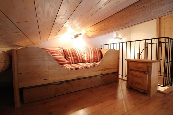 A loft-style bedroom with a wooden bunk bed, a small wooden dresser, and a metal railing.
