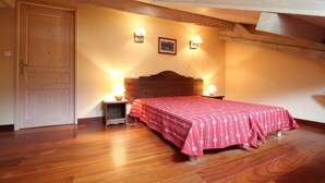 Un dormitorio con piso de madera, una cama con cubrecama rojo, dos lámparas de noche, cabecera de madera y una puerta.