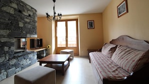Una sala de estar con pared de piedra, sofá de madera, televisor y candelabro.