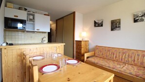 A compact living space with a kitchenette, a dining table with chairs, a sofa, and a lamp.