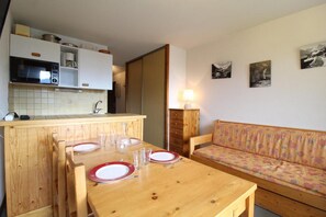 Um espaço compacto com cozinha compacta, uma mesa de jantar com cadeiras, um sofá e uma luminária.